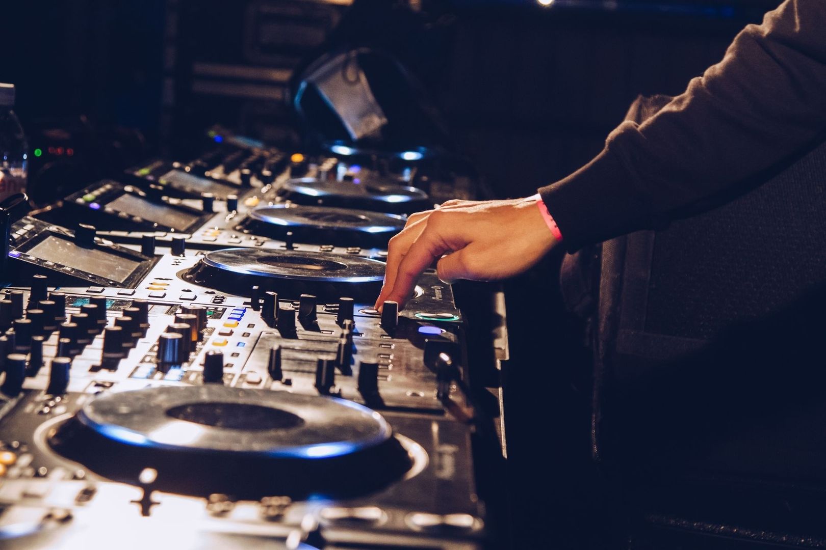 DJ adjusting controls on a multi-deck mixer in a dim venue